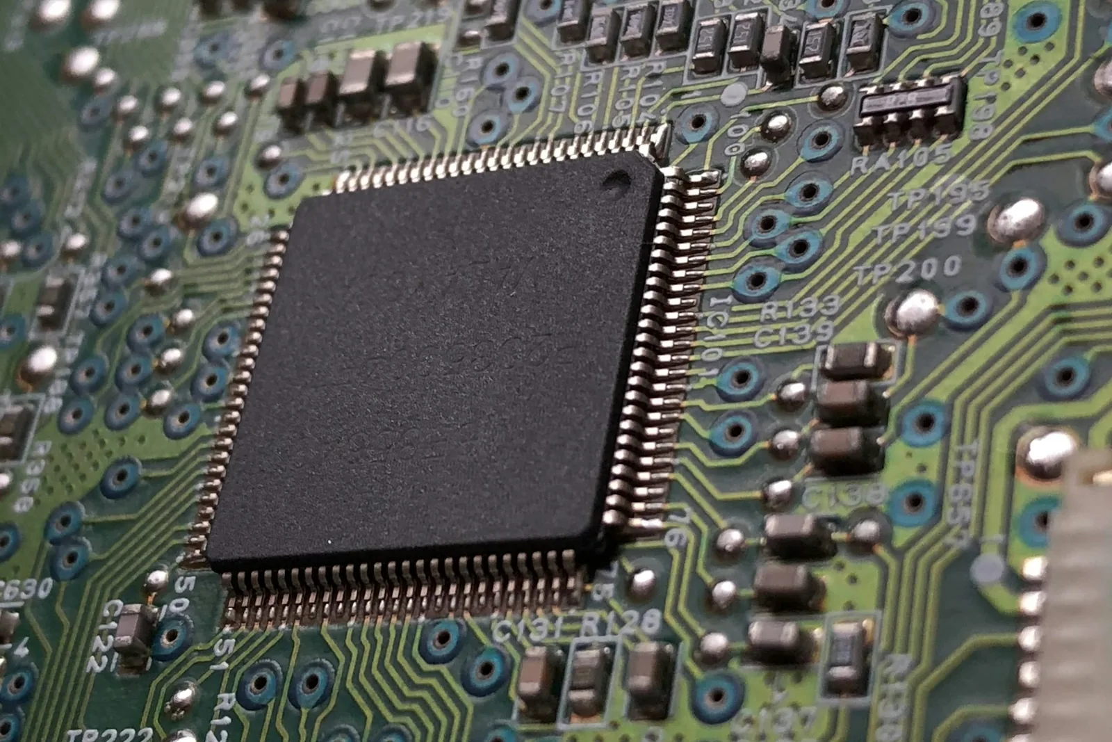 A chip soldered on a green circuit board, its pins and the components around it