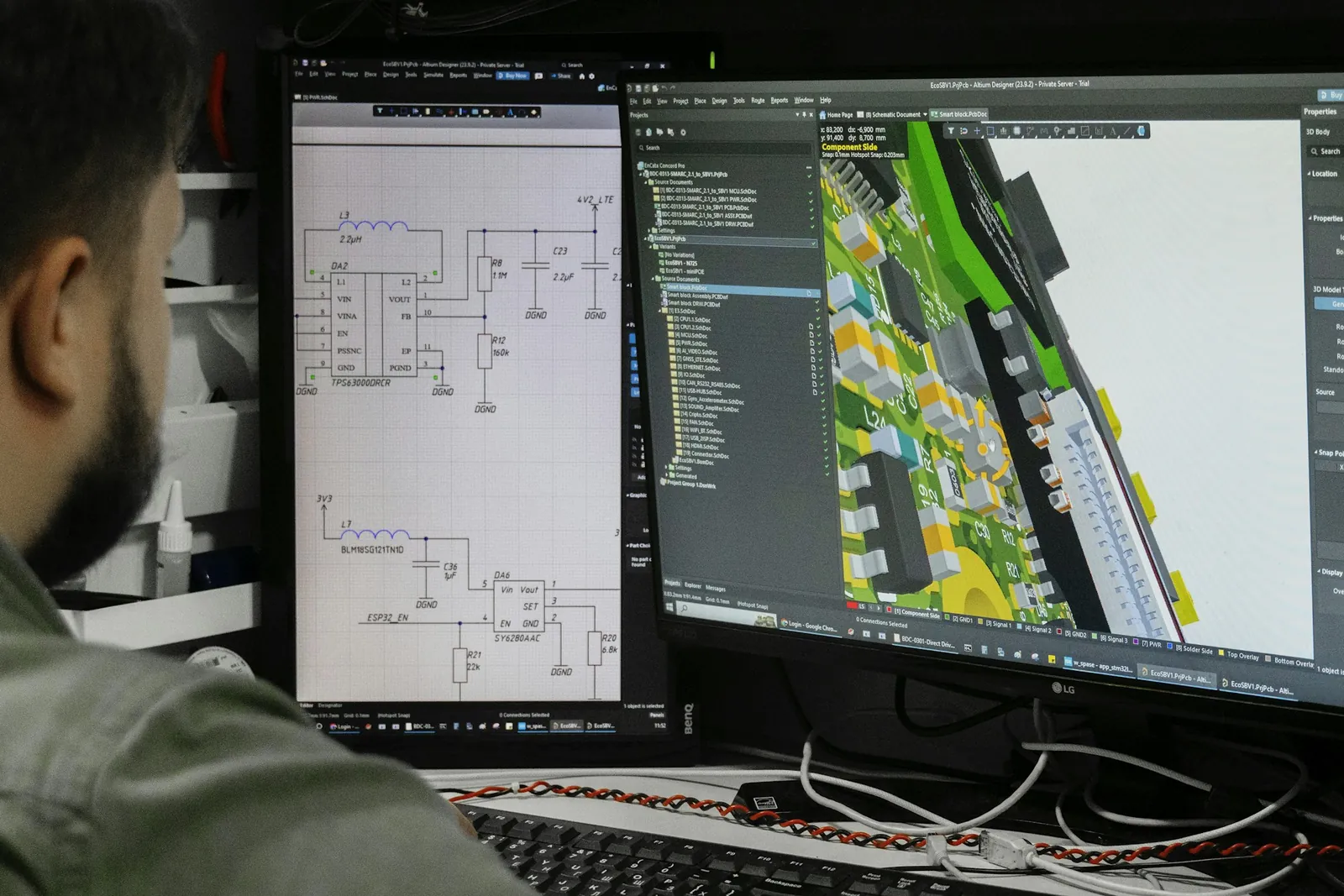 An engineer reviewing a schematic and the layout of its board on two screens